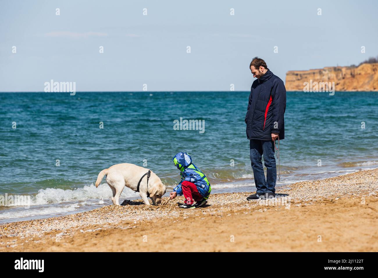 Vater und Sohn spielen im Winter mit einem Hund am Strand Stockfoto