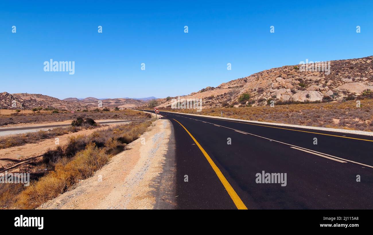 Asphaltierte Autobahn, die durch die trockene, trockene Landschaft der Namib-Wüste in Namibia führt Stockfoto