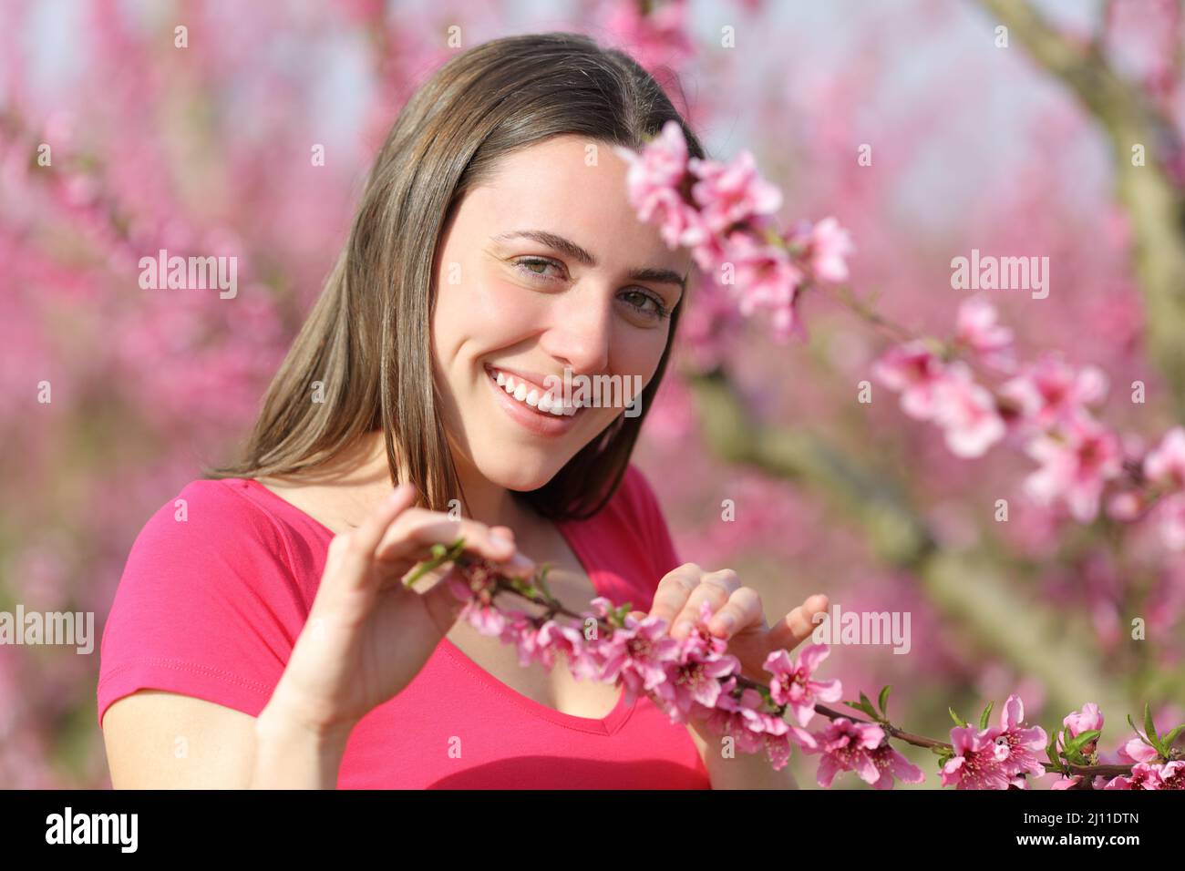 Offene Frau lächelt der Kamera zu, die mit Blumen in einem rosa Feld spielt Stockfoto