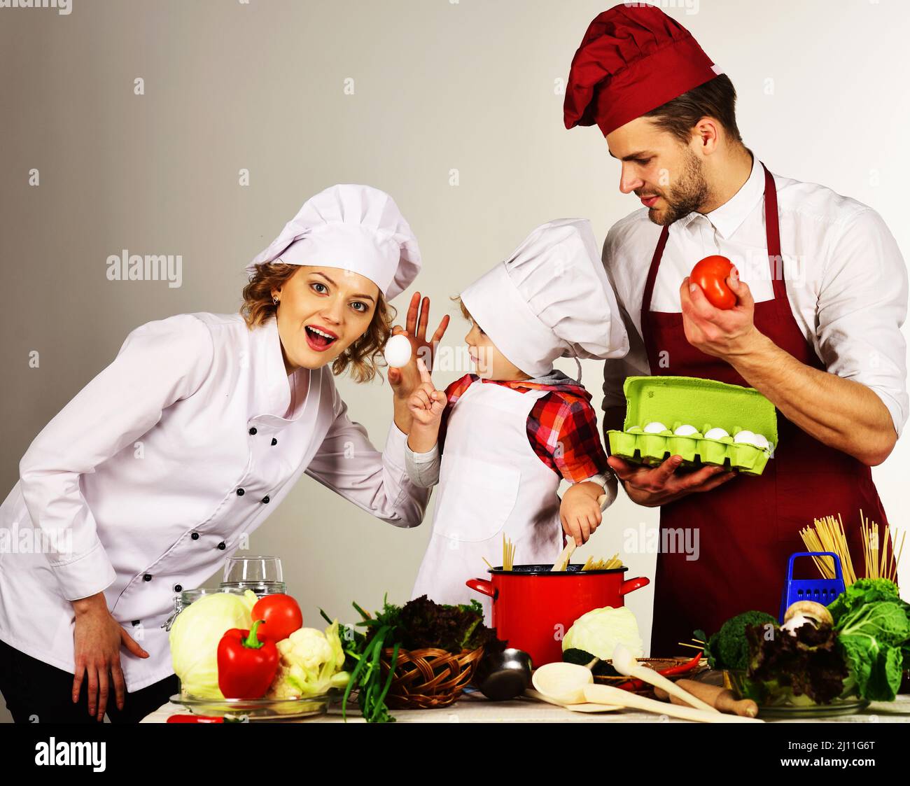 Glückliche Familie in der Küche. Niedliches Kind und Eltern im Kochhut. Mutter und Vater lehren Sohn, wie man kocht. Stockfoto