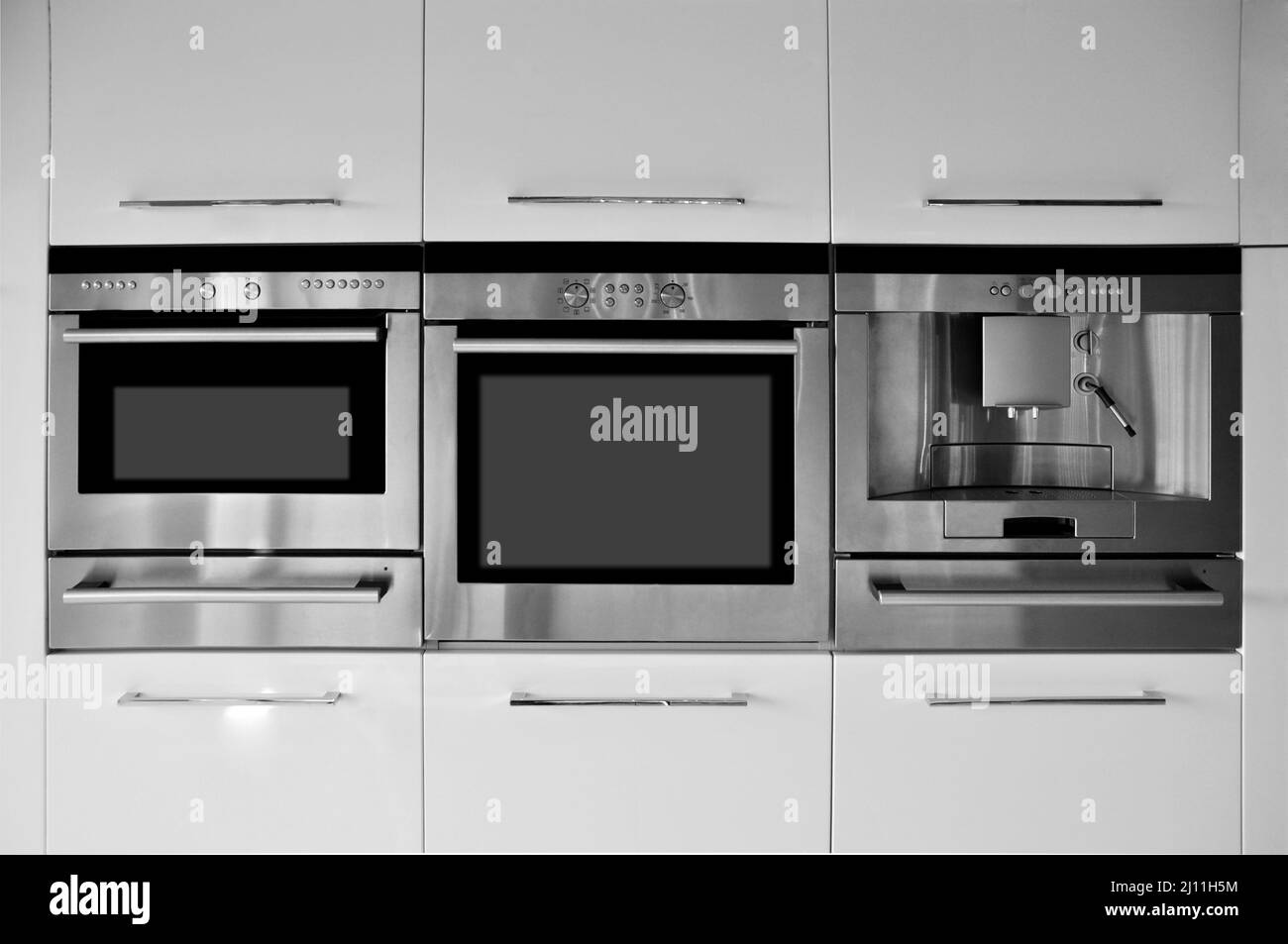 Interieur mit luxuriöser moderner Küchenausstattung, beigefarbenen Lackschränken, eingebautem Backofen und Kaffeemaschine Stockfoto