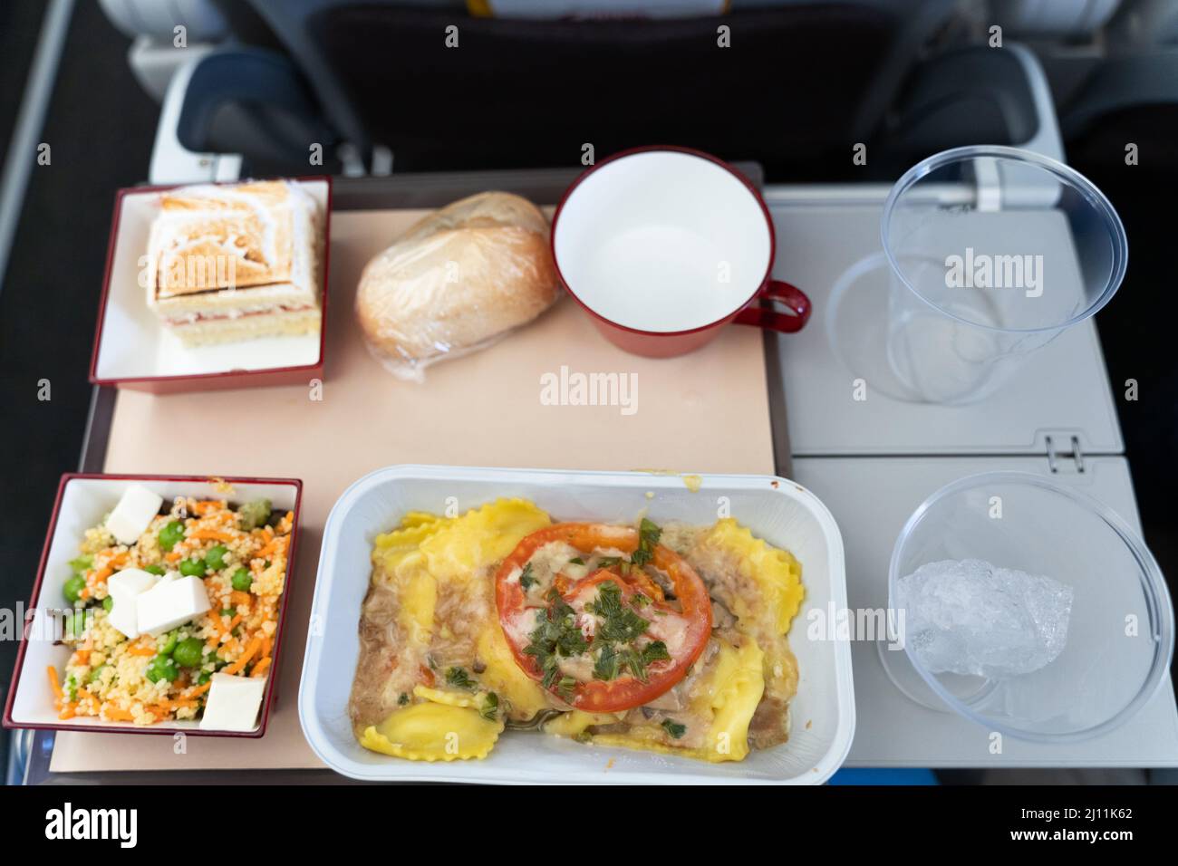 Flugzeug-Food-Menü auf Tablett. Vegetarische Mahlzeit mit Pasta, Salat, Kuchen, Brot und leeren Plastikgläsern im Flugzeug Stockfoto