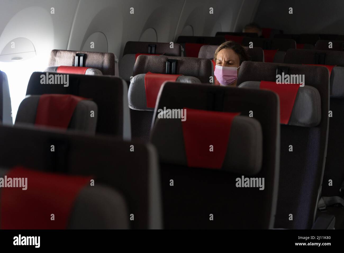 Frau mit rosa Gesichtsmaske sitzt auf Flugzeug-Reihensitz. Einsame Passagierin im Flugzeug, die in der Pandemiesaison unterwegs ist Stockfoto