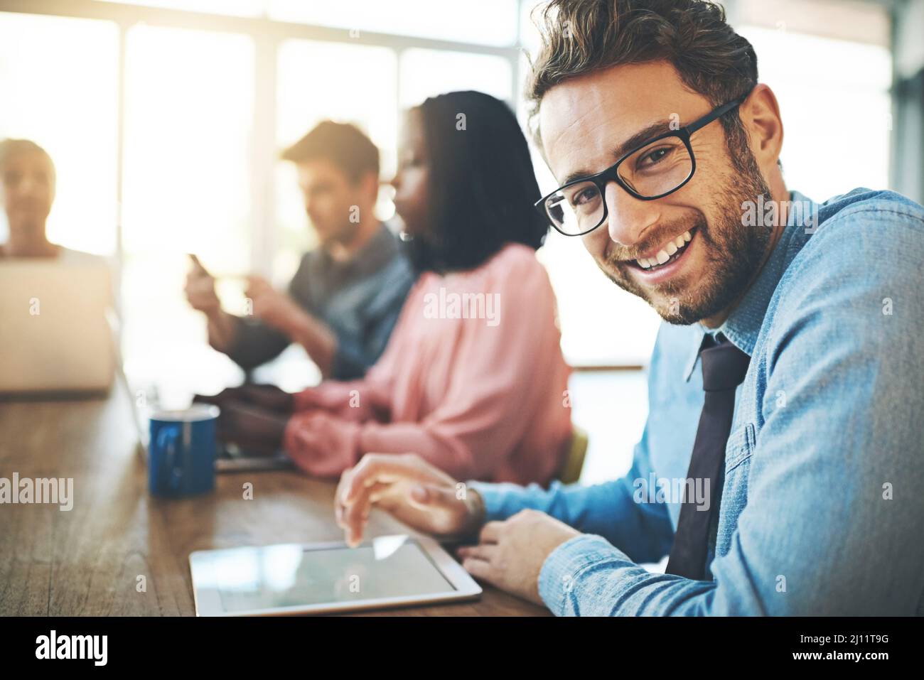 Optimistischer Blick auf die Zukunft seiner Karriere. Porträt eines Geschäftsmannes mit einem digitalen Tablet und seinen Kollegen im Hintergrund. Stockfoto
