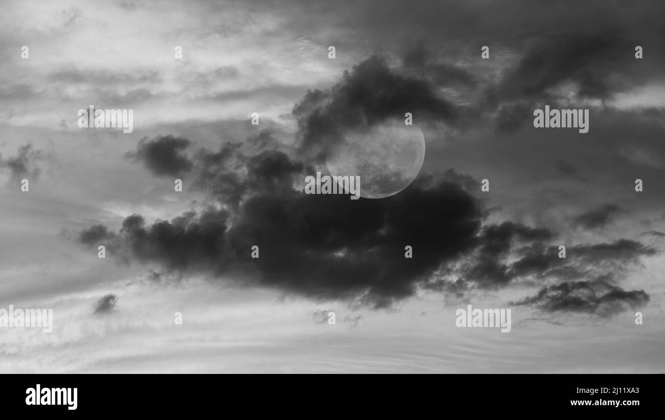 Ein Vollmond ist in Wolken eingebettet in Ein Moody 16: 9 Bildverhältnis hochauflösendes Schwarz-Weiß-Bild Stockfoto
