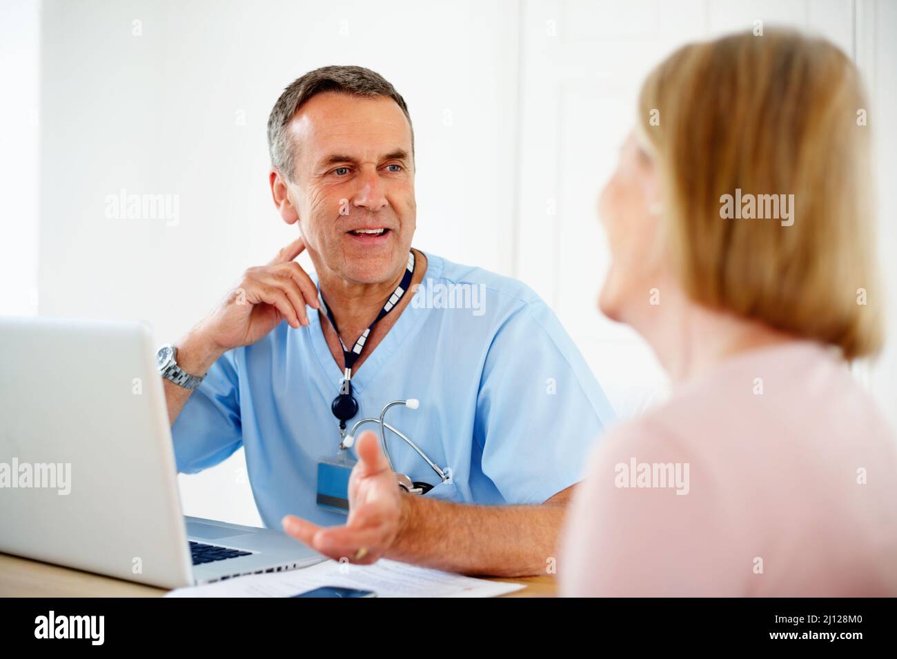 Reifer Arzt im Gespräch mit einer Patientin, die am Schreibtisch sitzt. Porträt einer reifen Ärztin im Gespräch mit einer Patientin, die am Schreibtisch sitzt. Stockfoto