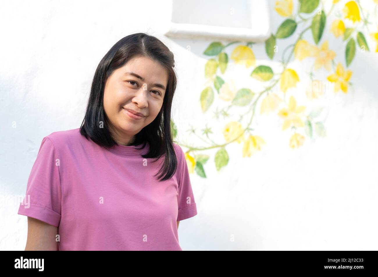 Porträt einer asiatischen Frau mittleren Alters mit weißer Wand eines Hausresorts und Vintage-Stil zur Dekoration gemalt, lächelndes Gesicht, kurze schwarze Haare Stil, Stockfoto