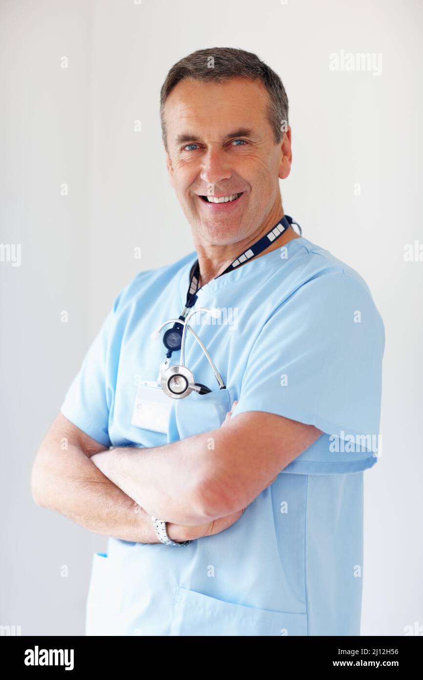 Selbstbewusster Arzt mit gefalteten Händen gegen Weiß. Porträt eines lächelnden Arztes mit gefalteten Händen vor weißem Hintergrund. Stockfoto