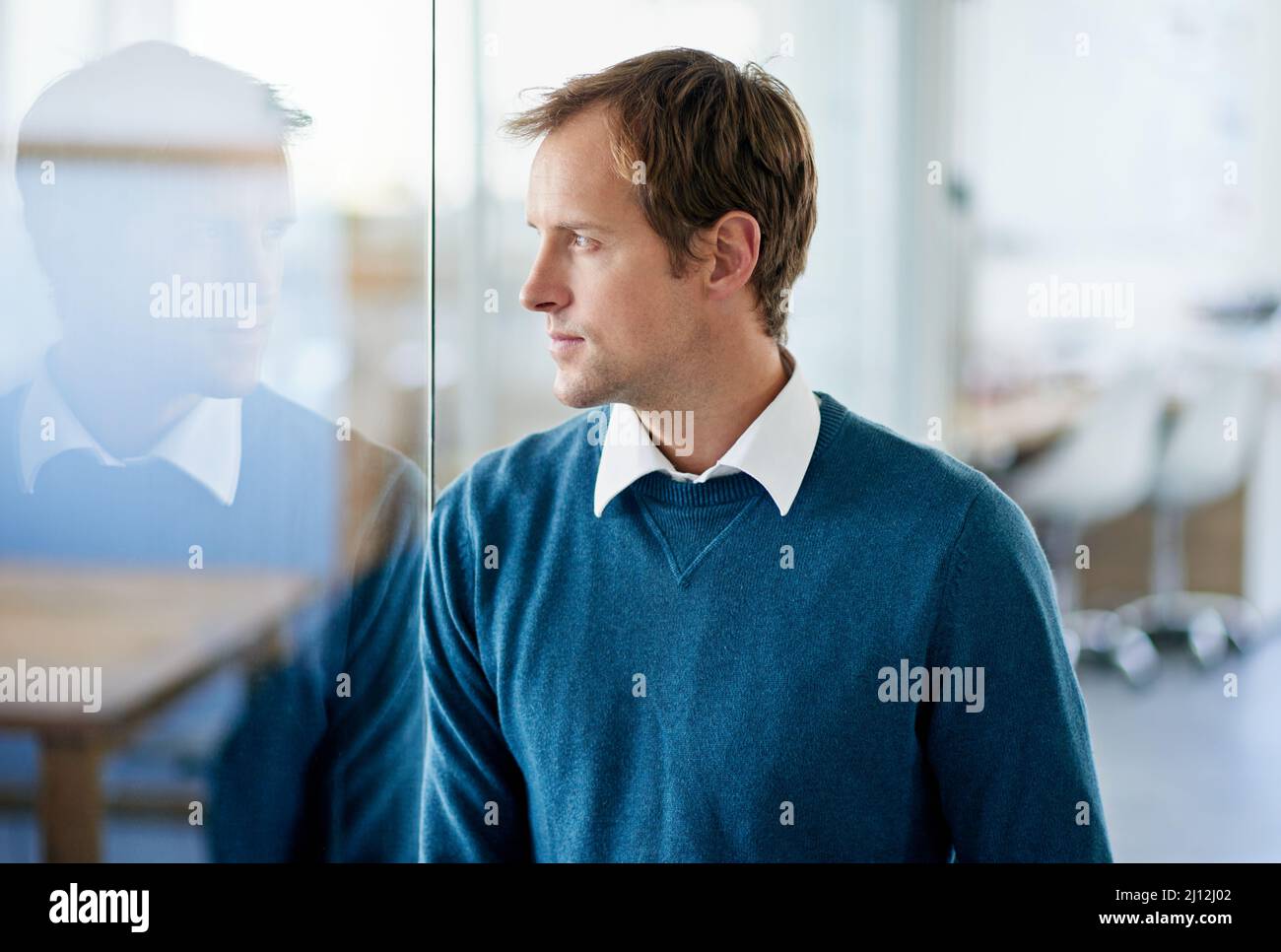 Harte Entscheidungen erfordern härteres Denken. Aufnahme eines hübschen Geschäftsmanns, der durch ein Glasfenster in ein Büro schaut. Stockfoto