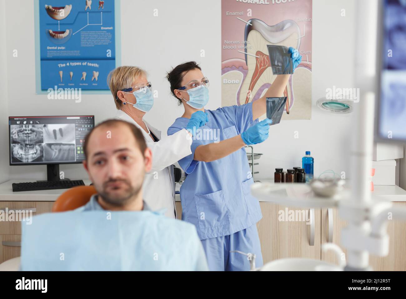 Porträt eines Patienten mit Zahnschmerzen, der während der stomatologischen Konsultation im Büro der Zahnmedizin auf einen medizinischen Eingriff wartet. Im Hintergrund medizinisches Team analysiert Zähne Radiographie. Medizinservice Stockfoto
