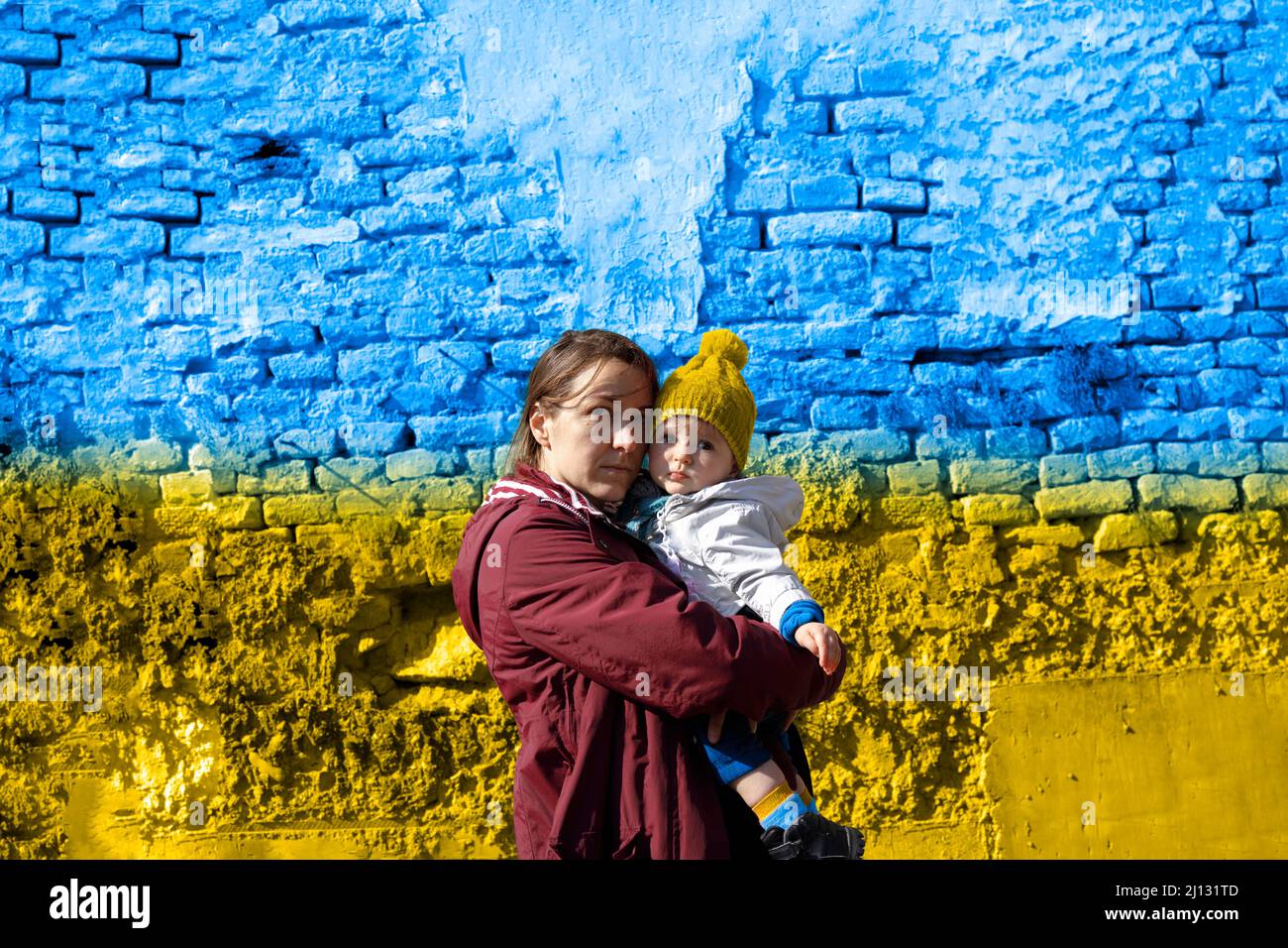 Verängstigte Frau, die ihr Kind vor die ukrainische Flagge hält Stockfoto