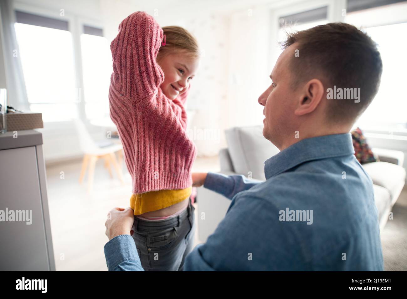 Vater half seiner kleinen Tochter mit Down-Syndrom, zu Hause Hosen zu tragen. Stockfoto