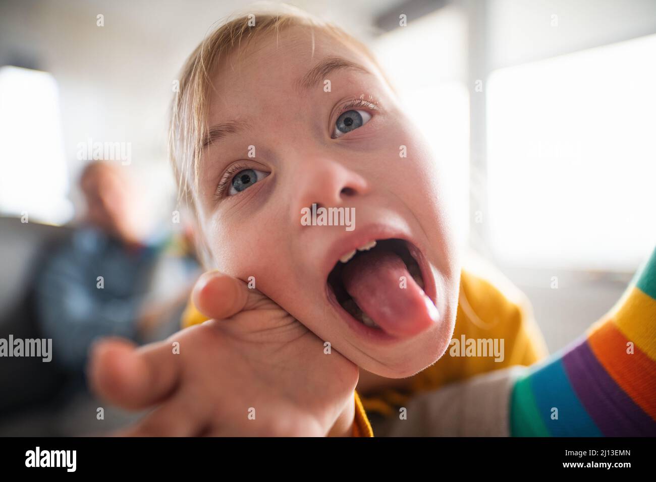 Nahaufnahme eines fröhlichen kleinen Mädchens mit Down-Syndrom, das zu Hause die Zunge herausstreckt. Stockfoto