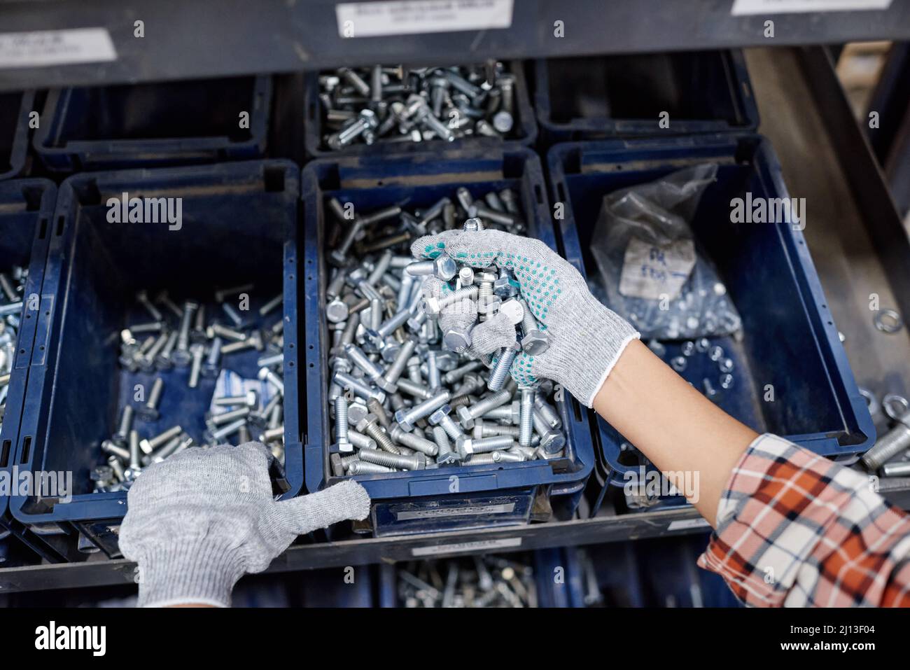 Über dem Winkel von Handschuhen einer weiblichen Maschinenbauerin, die während der Arbeit im Lager einen Haufen von Schrauben aus Edelstahl hält Stockfoto