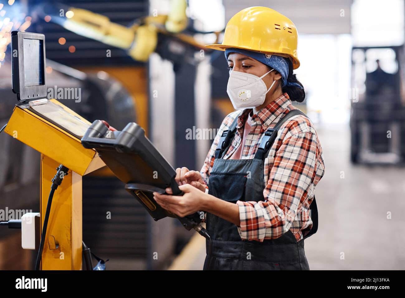 Zeitgemäßer Arbeiter der Industrieanlage in Overalls, Schutzhelm und Atemschutzmaske Schaltvorgänge für Produktionsmaschine Stockfoto
