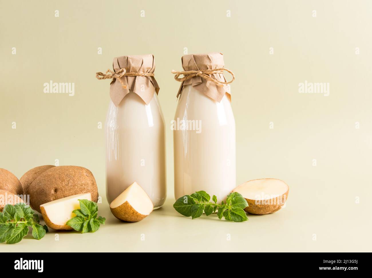 Zwei Glasflaschen mit veganer Pflanzenmilch aus Kartoffelknollen auf beigefarbenem pastellfarbenem Hintergrund. Das Konzept der gesunden Ernährung. Getränkersatz Stockfoto