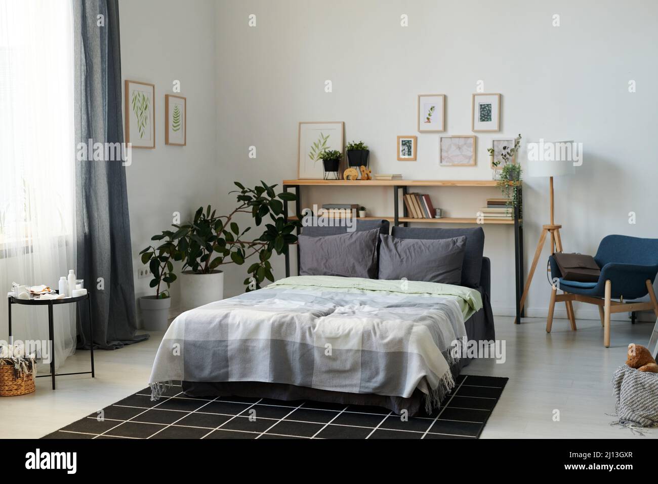 Teil eines geräumigen Schlafzimmers mit Doppelbett und Regalen in der Mitte, umgeben von Bildern in Rahmen an Wänden und heimischen Pflanzen Stockfoto