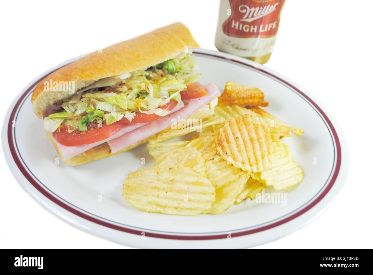 Ein Sub Sandwich mit Kartoffelchips serviert als kaltes Mittagessen mit einer Dose Miller Highllife Beer im Hintergrund Stockfoto