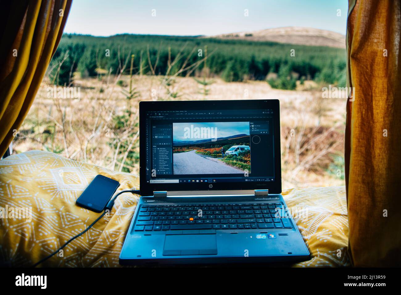 Von einem Wohnmobil aus unterwegs arbeiten das Leben eines digitalen Nomaden. Laptop und Telefon auf der Ausstellung mit Blick auf die schottische Landschaft. Reisefotografie Stockfoto