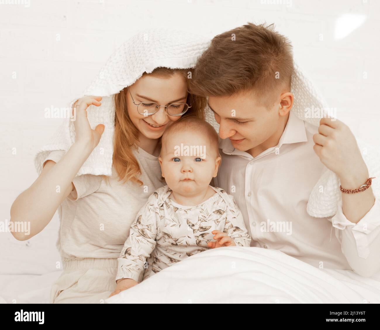 Portrait von fröhlich lächelnd glücklich Familie bedeckt weißes Handtuch. Frau, Mann, Baby, umarmt. Akzeptanz, Schutz. Nahaufnahme Stockfoto