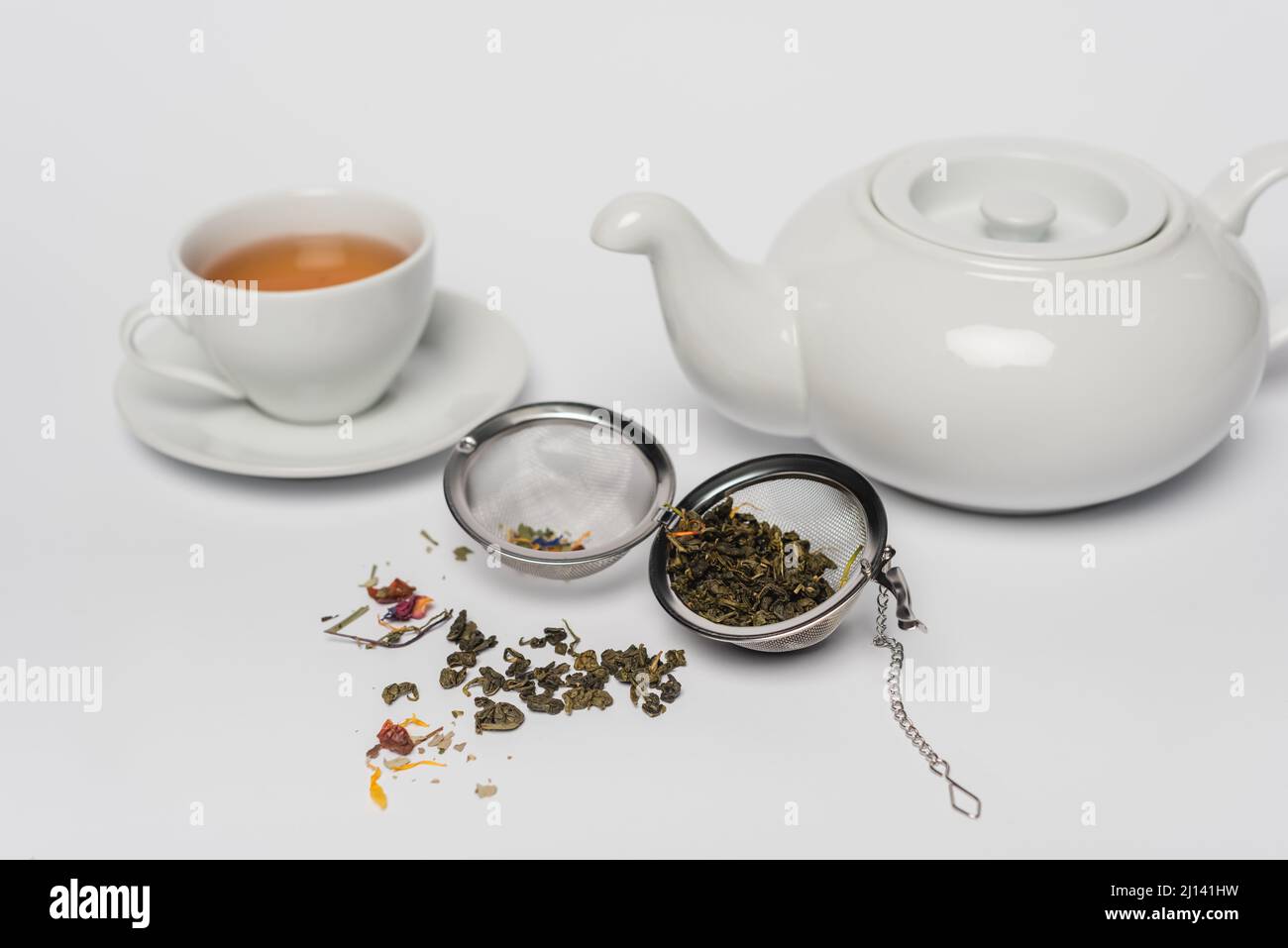 Trockener Tee im Infuser in der Nähe von Tasse und Teekannen auf weißem Hintergrund Stockfoto