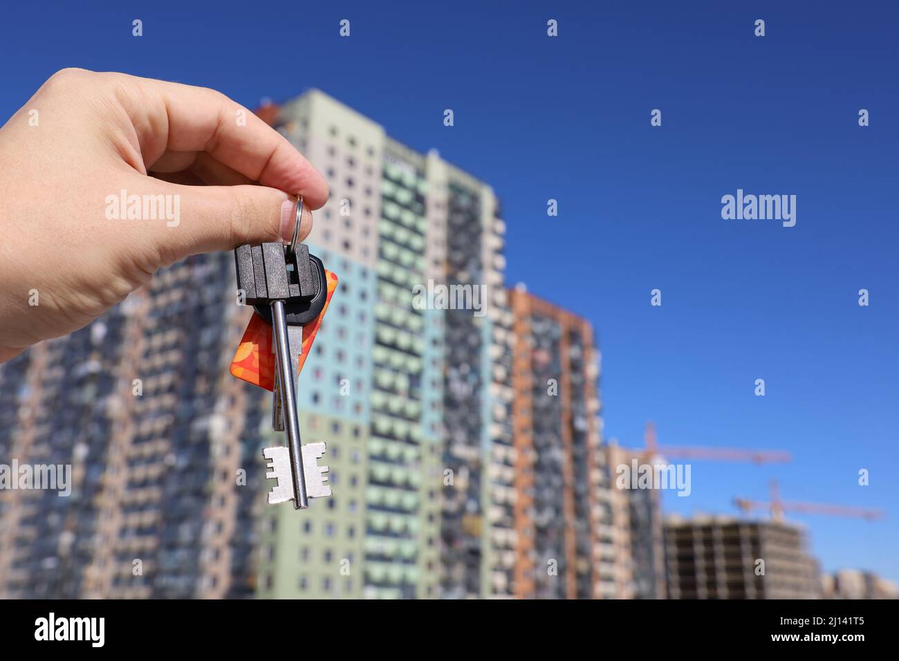 Wohnungskauf, männliche Hand mit Hausschlüsseln auf dem Hintergrund neuer Gebäude. Immobilienmakler, Umzug oder Vermietung von Immobilien Stockfoto