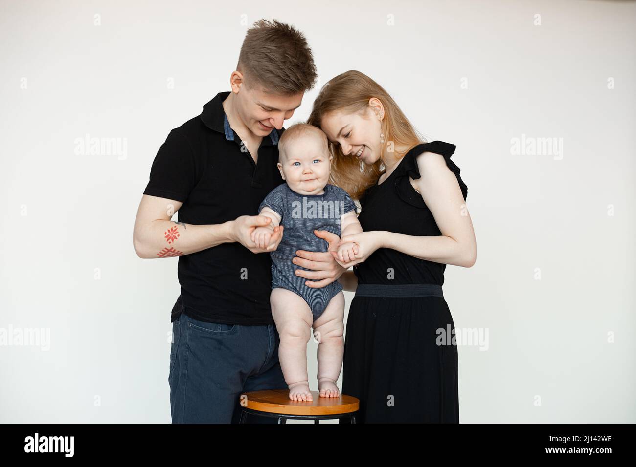 Glücklich lächelnd blonde traditionelle volle Familie mit Baby auf Stuhl, stehend, umarmen zusammen. Pflegen und Aufstehen. Stockfoto