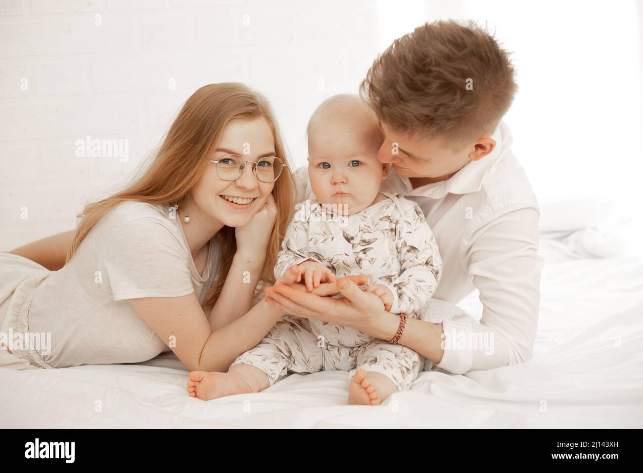 Glücklich fröhlich zufrieden Familie von Frau, Mann und Kleinkind in weißen Bettüberwürfen liegen. Familientag, Entwicklung von Kleinkindern Stockfoto