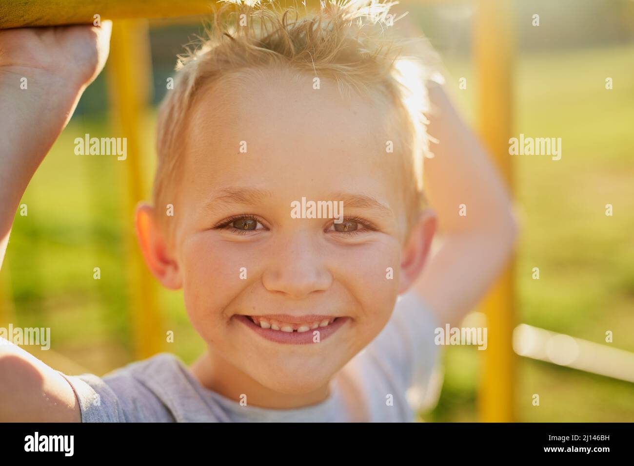 Fröhliche Kindheitstage. Porträt eines lächelnden kleinen Jungen, der in einer Dschungelturnhalle im Park spielt. Stockfoto