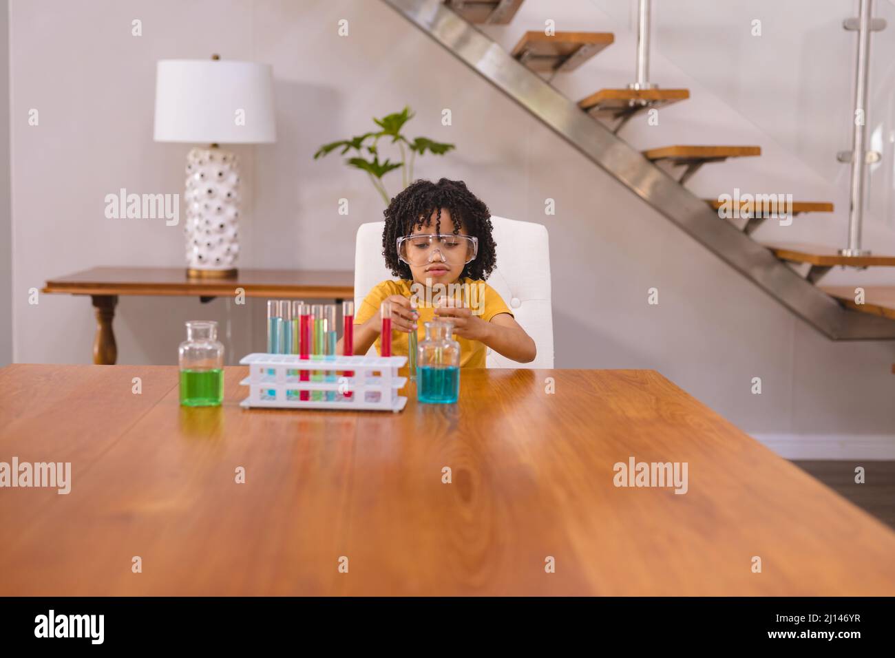 Hispanischer Junge mit Schutzbrille, der Chemikalien im Becher am Tisch mischt Stockfoto