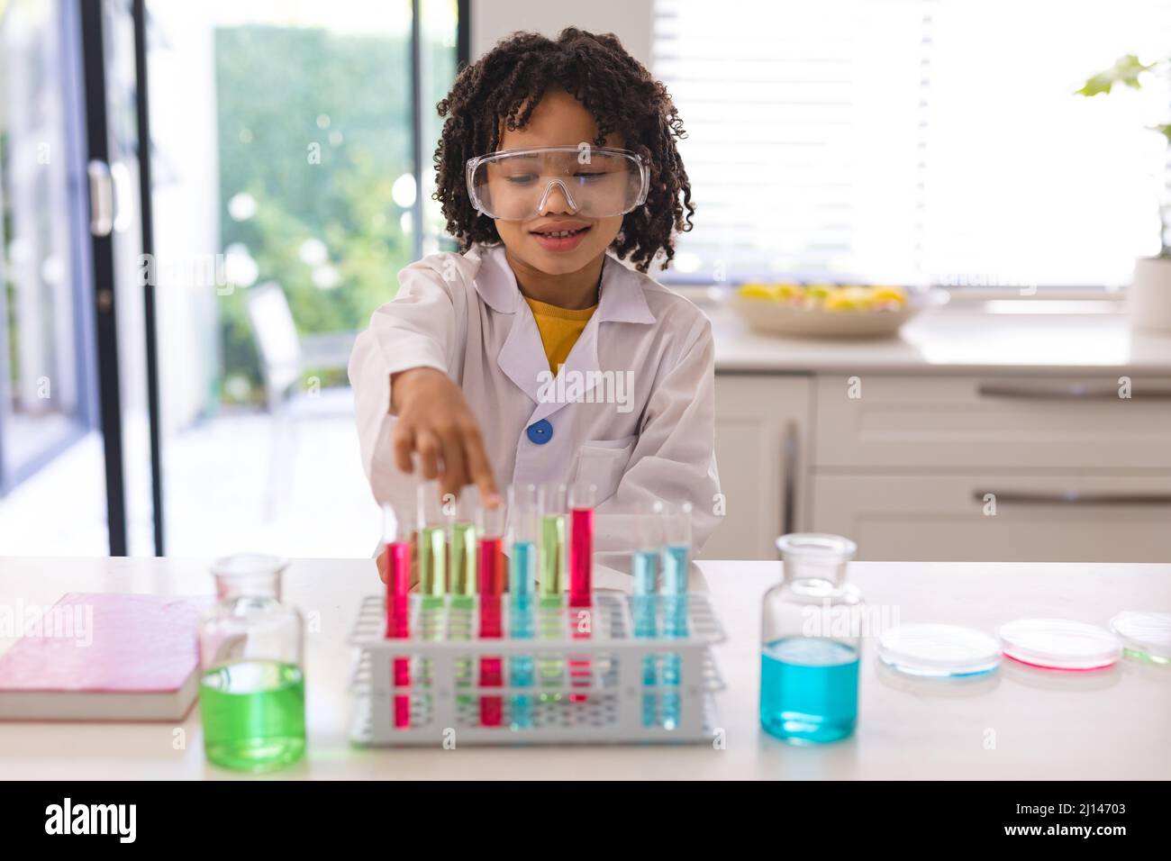 Netter lächelnder hispanischer Junge mit Schutzbrille, der wissenschaftliche Forschungen mit Chemikalien durchgeführt hat Stockfoto