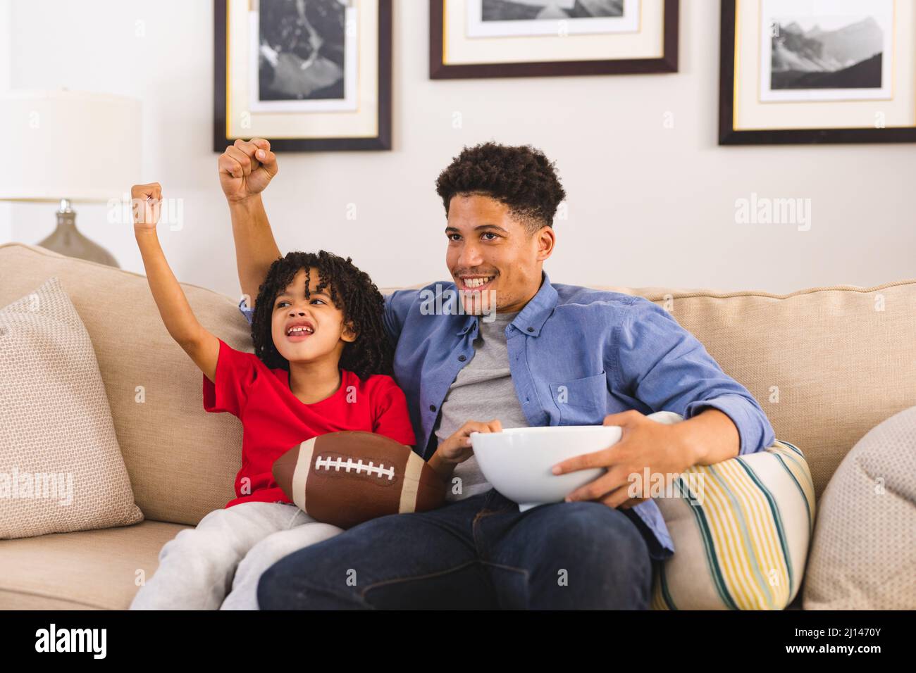 Aufgeregter hispanischer Vater und Sohn jubeln mit erhobenen Händen, während sie sich zu Hause ein Sportspiel im fernsehen ansehen Stockfoto