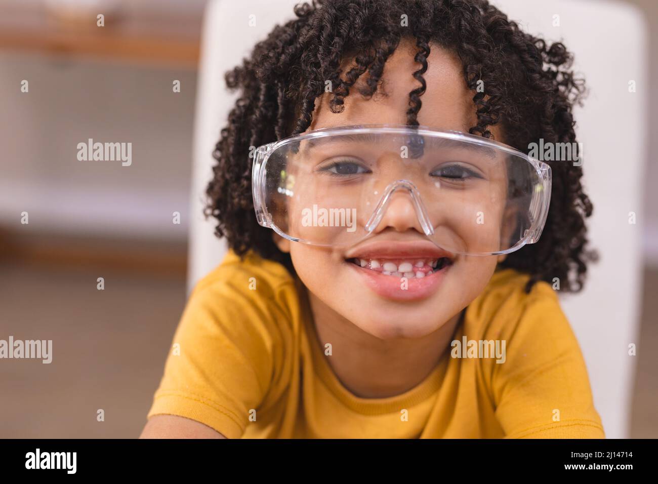 Porträt eines niedlichen lächelnden hispanischen Jungen mit lockigen schwarzen Haaren und Schutzbrille zu Hause Stockfoto