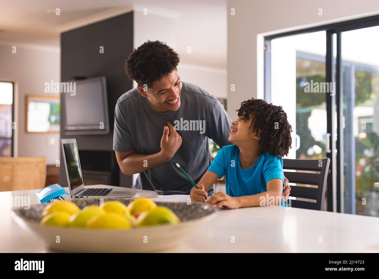 Glücklicher hispanischer Vater und Sohn reden, während Hausaufgaben in der Küche zu Hause machen Stockfoto