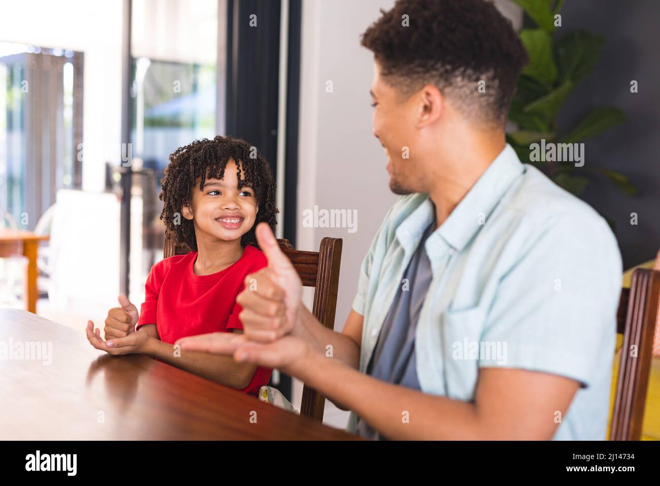 Glücklicher hispanischer Vater lehrt Zeichensprache, um Sohn stummzuschalten, während er am Esstisch sitzt Stockfoto