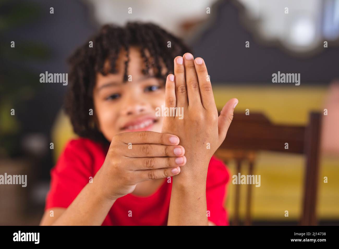 Porträt eines lächelnden hispanischen stummen Jungen, der ein Handzeichen zeigt, während er zu Hause sitzt Stockfoto