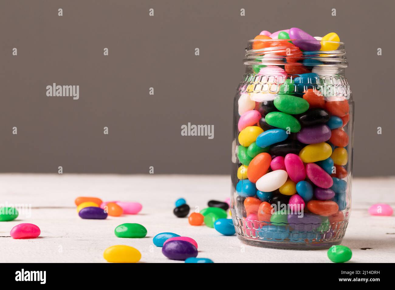 Nahaufnahme eines Vollglases mit mehrfarbigen Bonbons vor grauem Hintergrund mit Platz zum Kopieren Stockfoto