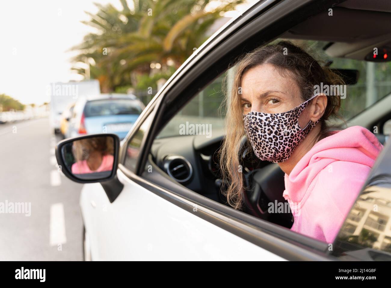 Frau mit Leopardenhaut Gesichtsmaske Blick nach hinten durch Autofenster. Fahrzeugmiete, Sicherheitsmassnahmen Konzepte Stockfoto