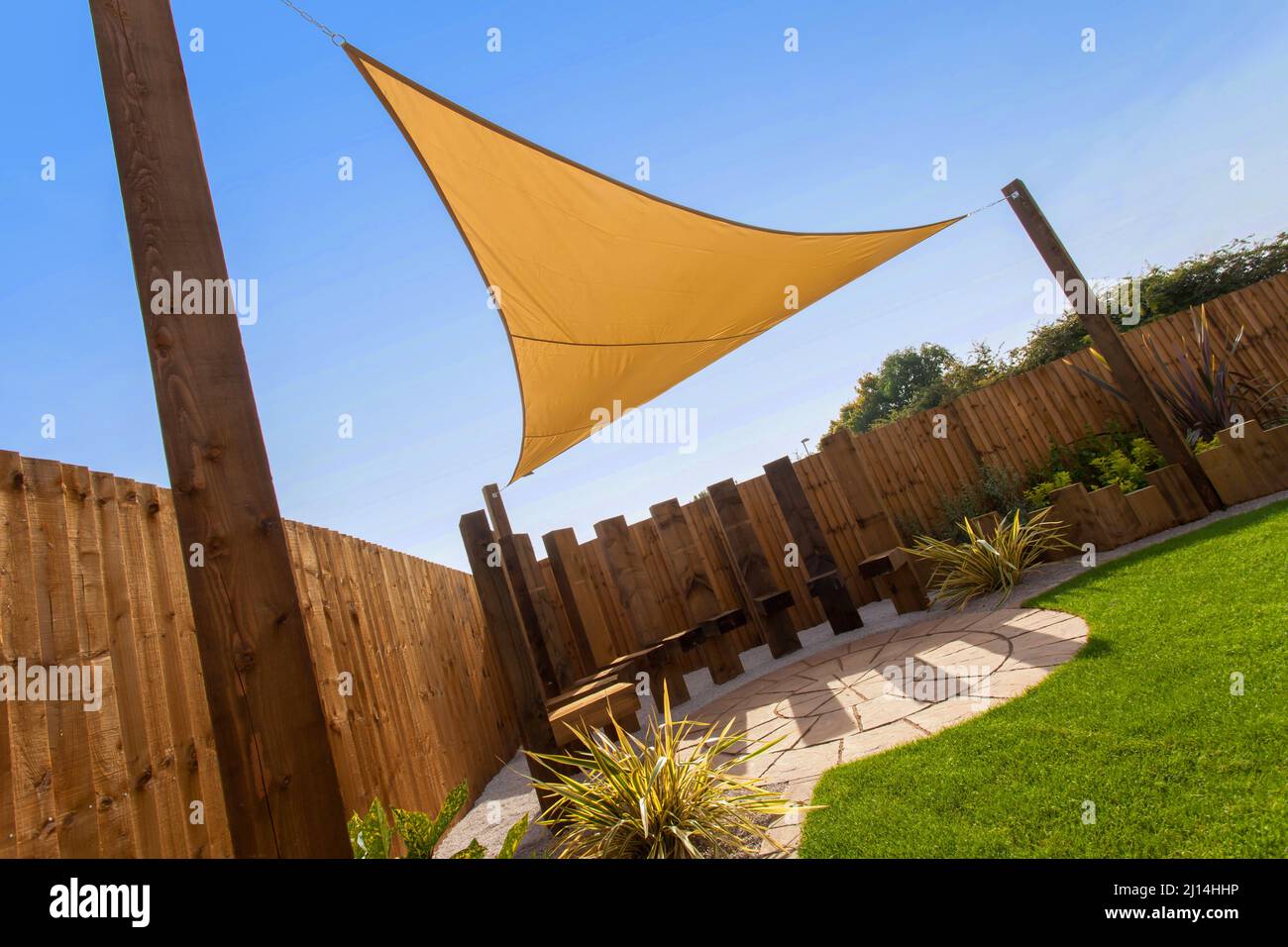 Ein gelber Sonnenschirm mit Drachen oder Segeln, der von Pfosten in einem sonnigen Garten und blauem Himmel unterstützt wird. Stockfoto