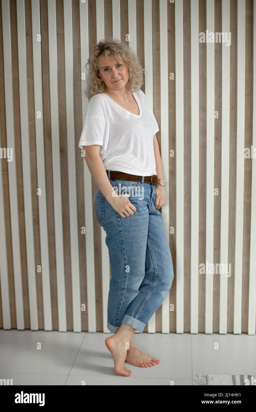 In voller Länge Porträt der blonden Spaß Erwachsene Frau. Weibchen steht neben einer Wand und posiert vor der Kamera Stockfoto