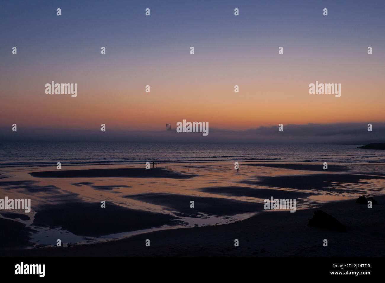 Sonnenuntergang über dem Praia de Sao Torpes mit Fischern, die bei Ebbe am Strand Muscheln sammeln, in der Nähe von Sines, Küste von Alentejo, Portugal. Stockfoto