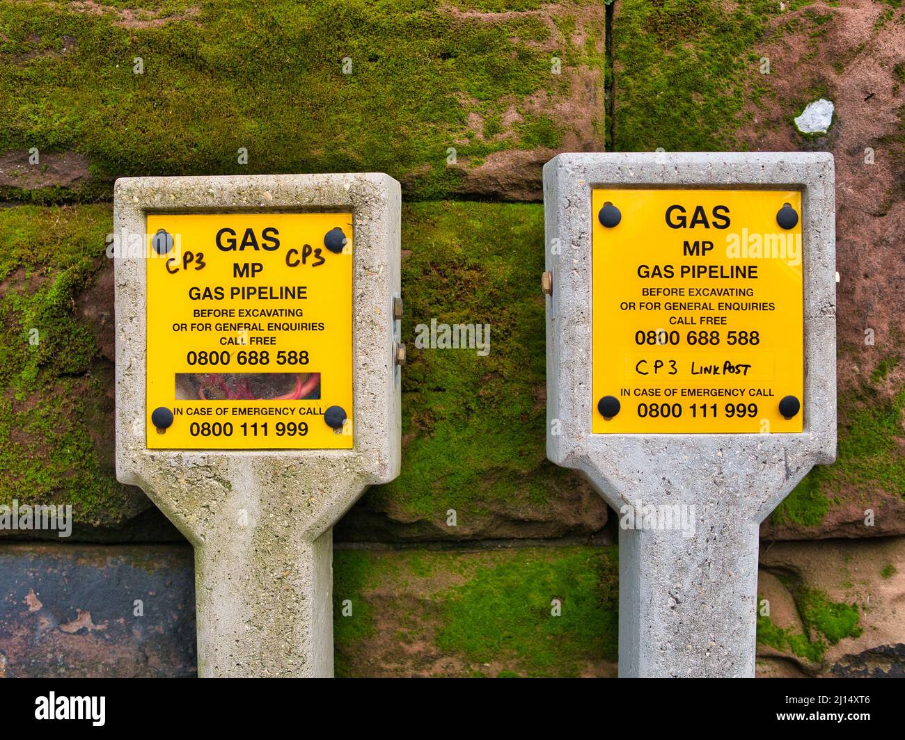 Gelbe Schilder auf Betonpfosten warnen vor Gasleitungen mit mittlerem Druck (MP) in einem städtischen Gebiet im Nordwesten Großbritanniens. Stockfoto