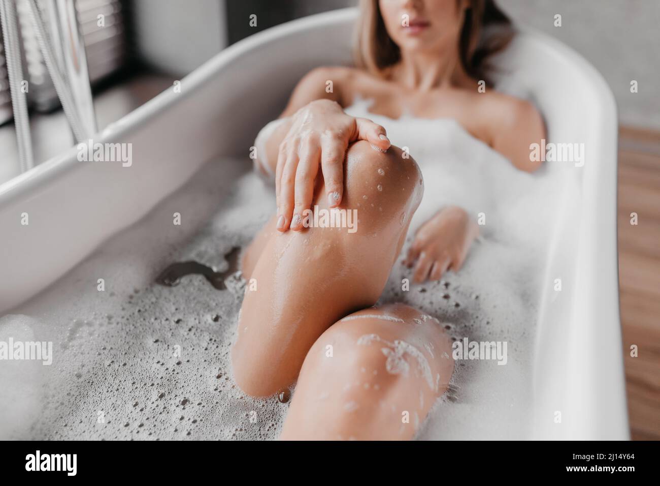 Verfahren zur Sauberkeit und häuslichen Schönheit. Junge Dame, die sich in der Badewanne entspannt und Schaum und berührende Beine genießt Stockfoto