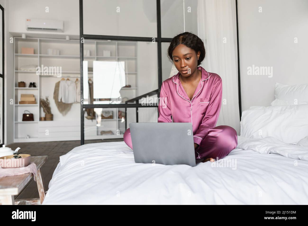 Serious Black Female Mit Laptop Websurfing Sitzen Auf Bett Innen Stockfoto