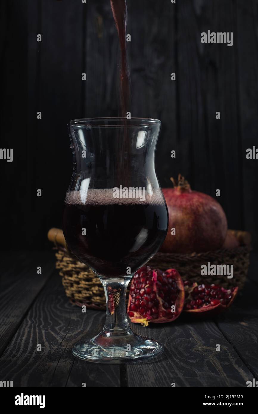 Ein Glas Granatapfelwein oder Saft vor einem Hintergrund reifer Früchte in einem Korb in einem dunklen Schlüssel Stockfoto