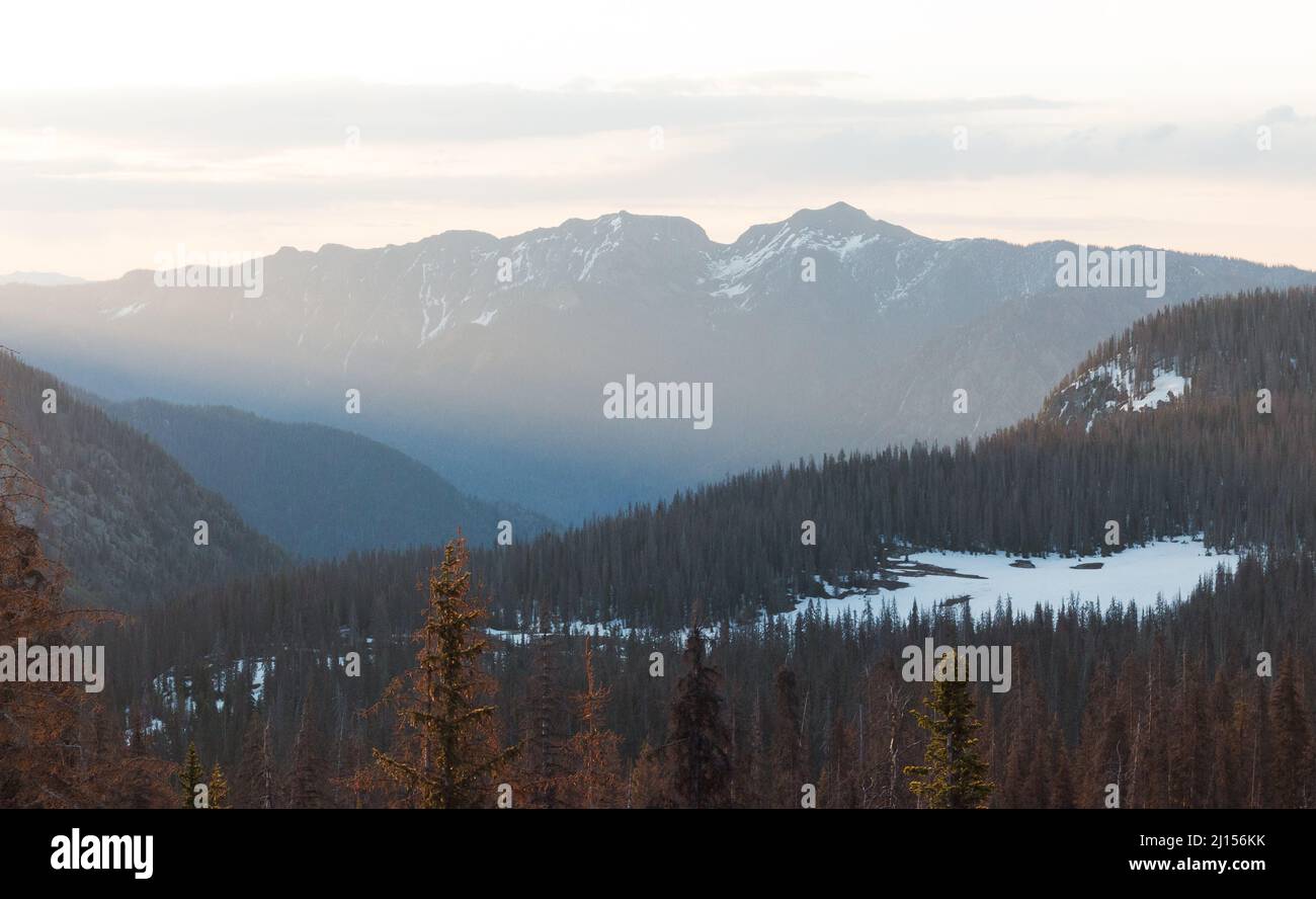 Mehrschichtige Berglandschaft bei Sonnenaufgang mit Sonnenstrahlen und Schnee Stockfoto