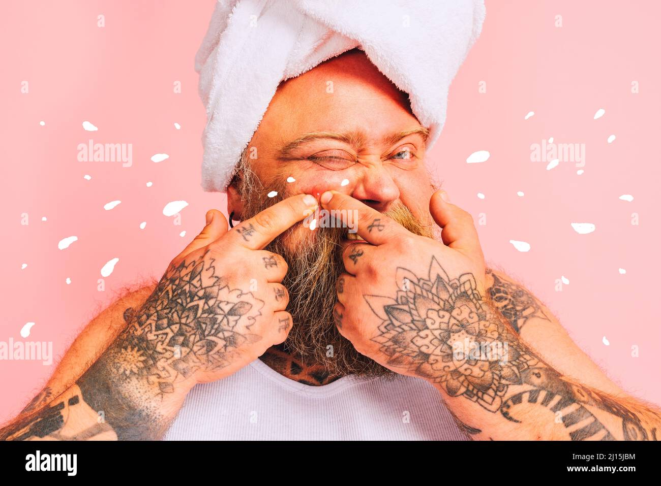 Mann mit Bart und Handtuch über dem Kopf quetscht einen Pickel Stockfoto