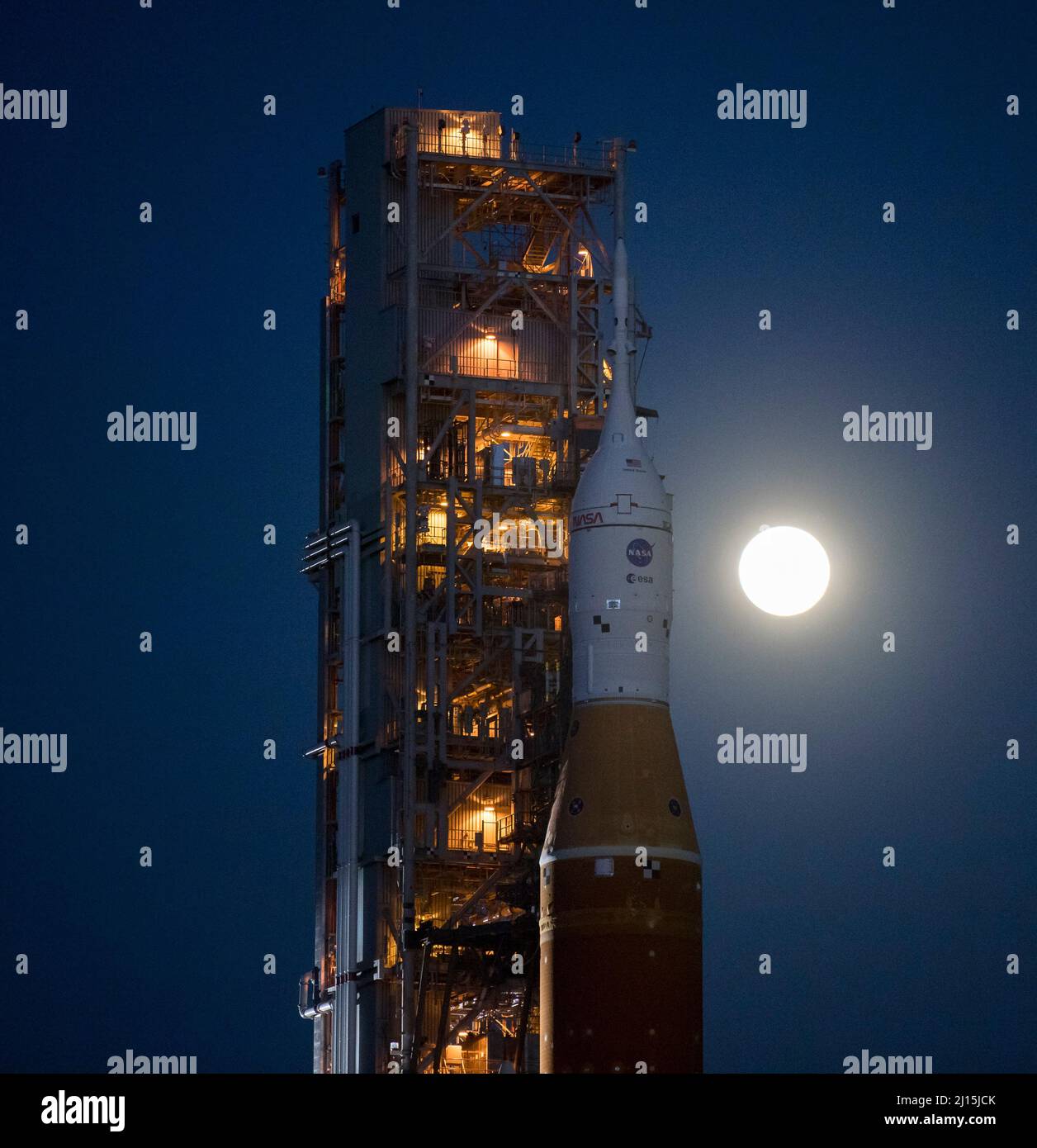 Der Mond steigt hinter der NASA-Rakete Space Launch System (SLS) mit der Orion-Sonde an Bord auf einem mobilen Trägerrakete auf, während er zum ersten Mal am Donnerstag, dem 17. März 2022, im Kennedy Space Center der NASA in Florida zum Launch Complex 39B ausrollt. Vor dem Artemis I-Flugtest der NASA werden die vollständig gestapelte und integrierte SLS-Rakete und die Orion-Raumsonde im Launch Complex 39B einer Nassprobe unterzogen, um die Systeme zu verifizieren und Countdown-Verfahren für den ersten Start zu üben. Bildnachweis: (NASA/Aubrey Gemignani) Stockfoto