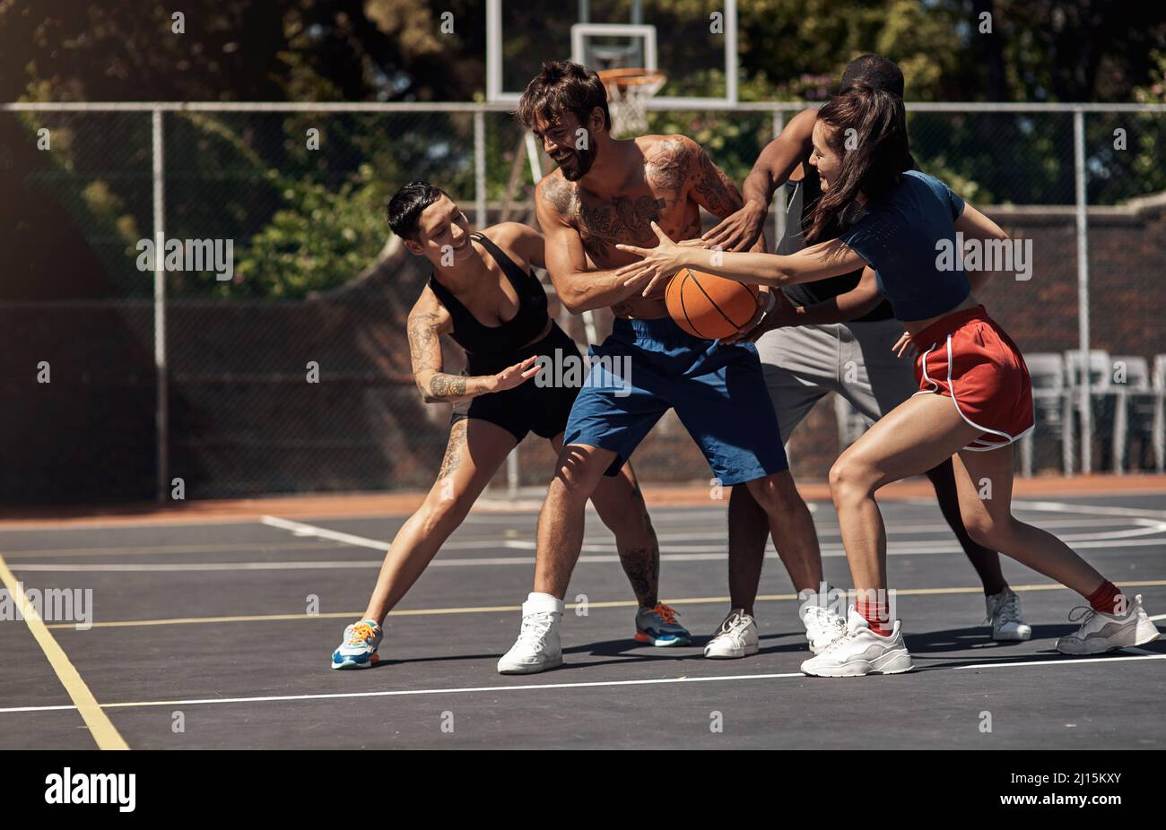 Sie können Basketball mit einem spielerischen oder wettbewerbsorientierten Geist spielen. Aufnahme einer Gruppe sportlicher junger Menschen, die auf einem Sportplatz Basketball spielen. Stockfoto