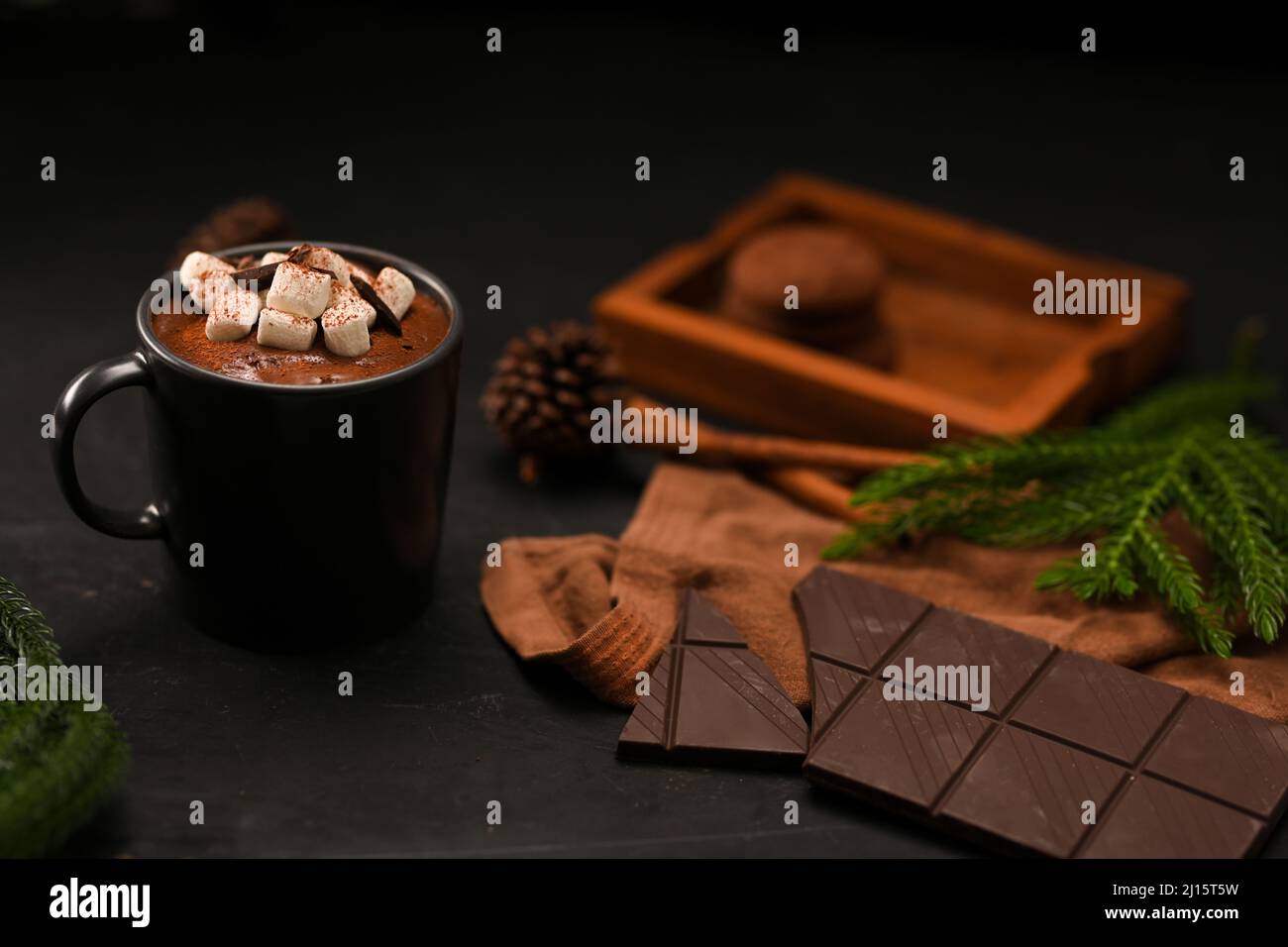 Hausgemachte heiße dunkle Schokoladenmilch mit Marshallows in einem schwarzen Keramikbecher, Schokoriegel und Dekorationen auf schwarzem Hintergrund. Stockfoto